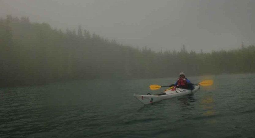 a student paddles a kayak through fog